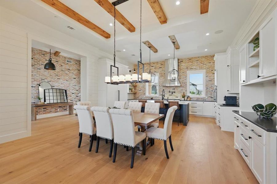 Dining space with beam ceiling, light wood-style flooring, and brick wall Dining space with beam ceiling, light wood-style flooring, and brick wall