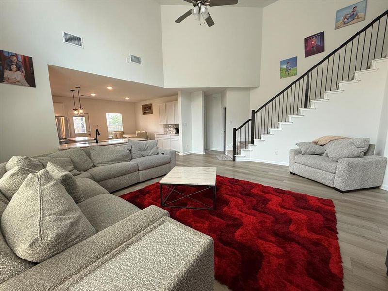 Open-concept living space featuring high ceilings, light-tone flooring, and a modern staircase with black iron balusters