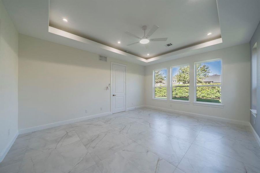 Empty room with a tray ceiling, light marble finish floors, ceiling fan, and recessed lighting Empty room with a tray ceiling, light marble finish floors, ceiling fan, and recessed lighting
