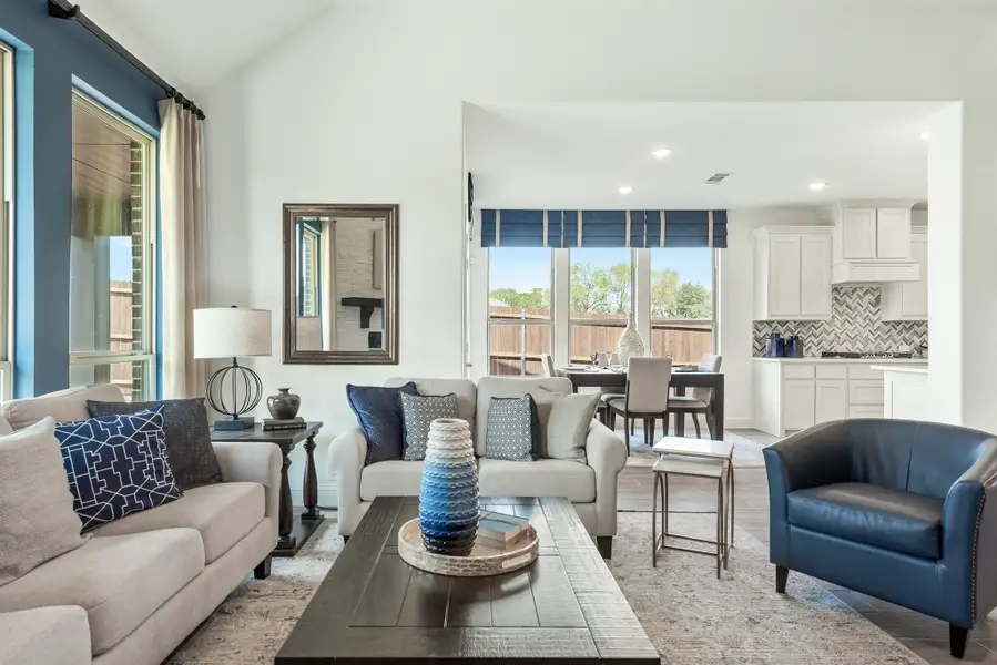 Open-concept living room with gray sofas, blue accents, and kitchen visible in background