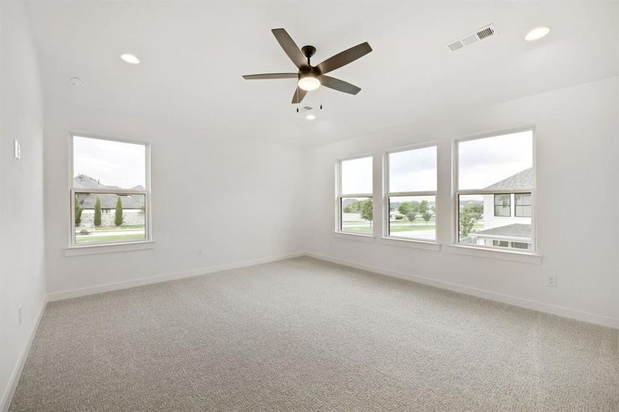 Spacious room featuring light-colored carpeting, multiple windows providing ample natural light, a ceiling fan with integrated lighting, and recessed ceiling lights Spacious room featuring light-colored carpeting, multiple windows providing ample natural light, a ceiling fan with integrated lighting, and recessed ceiling lights