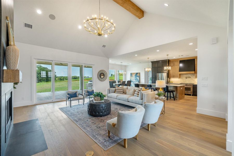 Living area with a chandelier, recessed lighting, high vaulted ceiling, light wood finished floors, and a fireplace with flush hearth