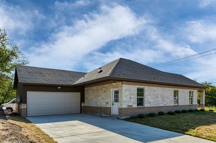 View of home's exterior with roof with shingles, concrete driveway, an attached garage, and stone siding View of home's exterior with roof with shingles, concrete driveway, an attached garage, and stone siding