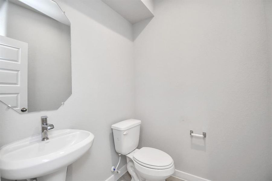 The half bathroom, conveniently situated on the 1st floor, is adorned with contemporary finishes. Pedestal sink, custom wall paint, and a sleek faucet combine to create a bright and inviting space. Sample photo, as built color and selections will vary.