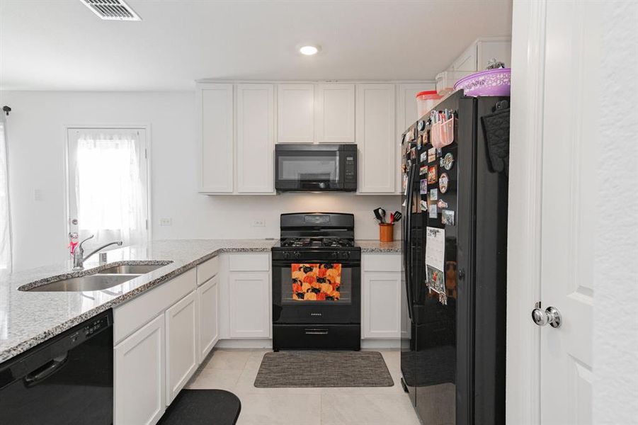 Kitchen featuring black appliances, white cabinets, light stone countertops, light tile patterned floors, and recessed lighting