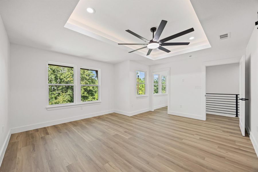 Different angle of primary bedroom with a raised ceiling, light wood-type flooring, recessed lighting, and ceiling fan