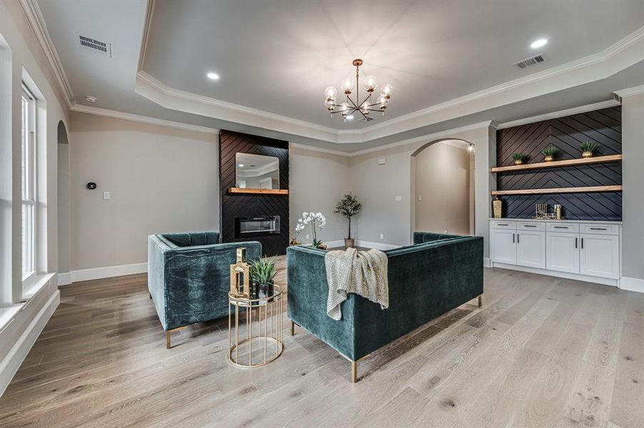 Living room featuring a tray ceiling, a fireplace, ornamental molding, a chandelier, and light wood-type flooring