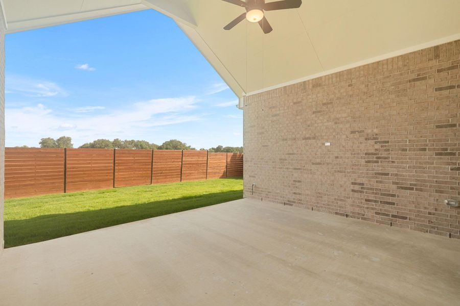 An inviting covered patio extends to a verdant lawn, privately enclosed by a stylish wooden fence.