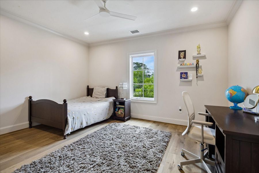 Charming large secondary bedroom featuring hardwood flooring, crown molding, recessed lighting, modern ceiling fan and a large divided light window that fills the space with natural light and serene views.