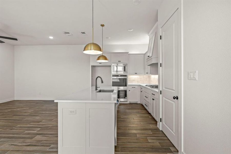 Kitchen featuring stainless steel microwave, a sink, dark wood-style floors, backsplash, and a kitchen island with sink
