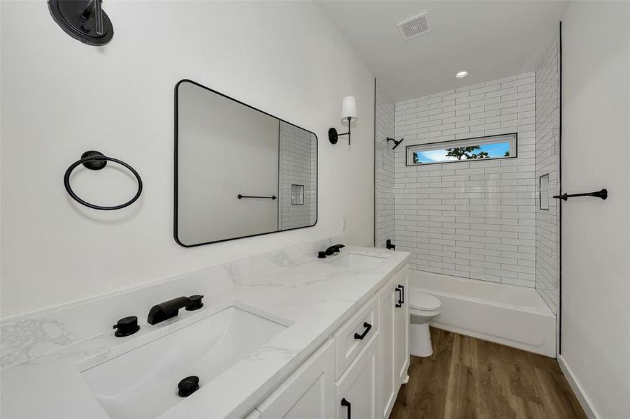 Bathroom with toilet, wood finished floors, washtub / shower combination, and double vanity Bathroom with toilet, wood finished floors, washtub / shower combination, and double vanity