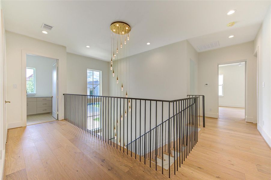 The expansive upstairs landing serves as both a functional living space and an architectural showcase, overlooking the dramatic two-story foyer below. Rich French Oak flooring flows continuously throughout the second level, creating a seamless sense of warmth, sophistication, and cohesion. Bathed in natural light and framed by sleek iron railings, this open gallery-style space enhances the home's airy design while providing an elegant transition between the upstairs living areas.