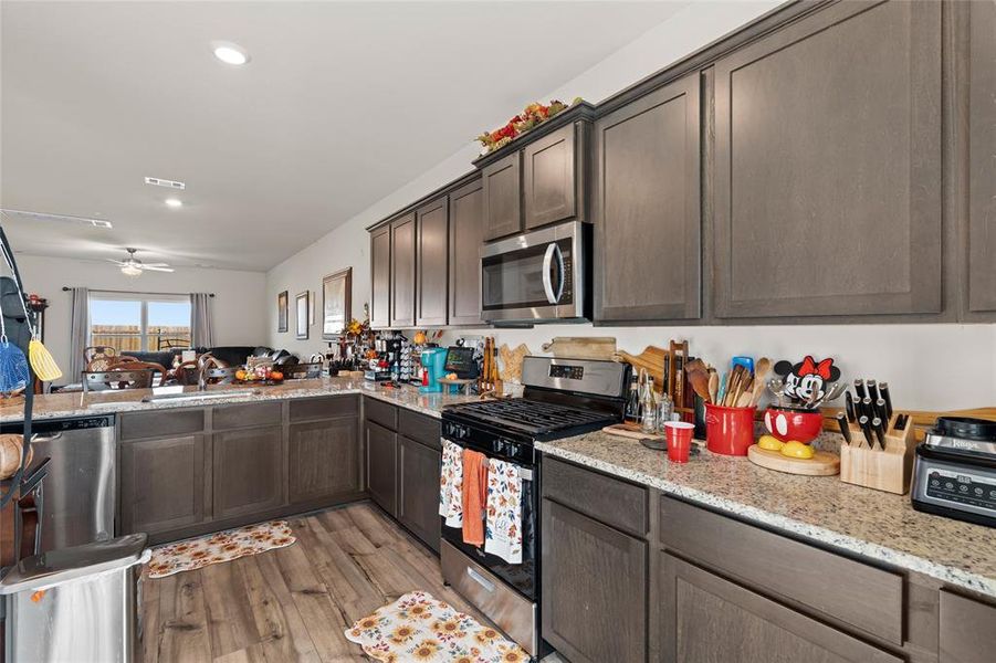 Kitchen featuring appliances with stainless steel finishes, open floor plan, light stone countertops, dark brown cabinetry, and recessed lighting