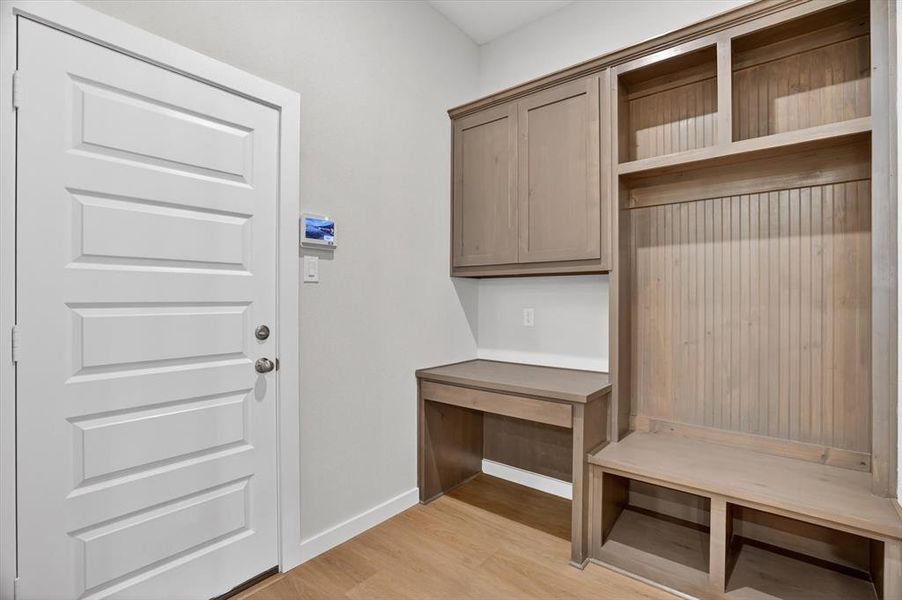 Mudroom featuring built-in cabinetry, an integrated desk, open shelving, a bench, and wood-finish flooring