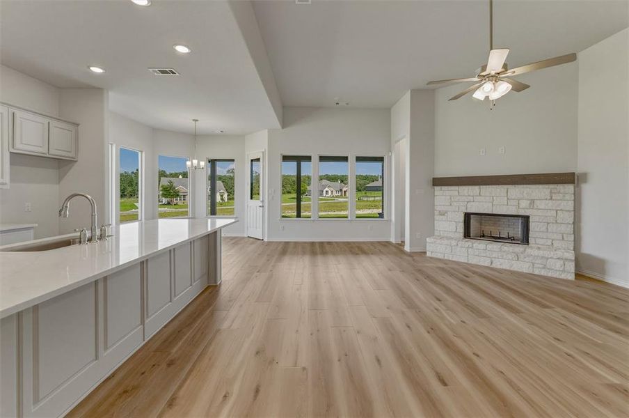 Spacious open-concept living area featuring wood-finish flooring, a stone fireplace with a wood mantle, and a ceiling fan Spacious open-concept living area featuring wood-finish flooring, a stone fireplace with a wood mantle, and a ceiling fan