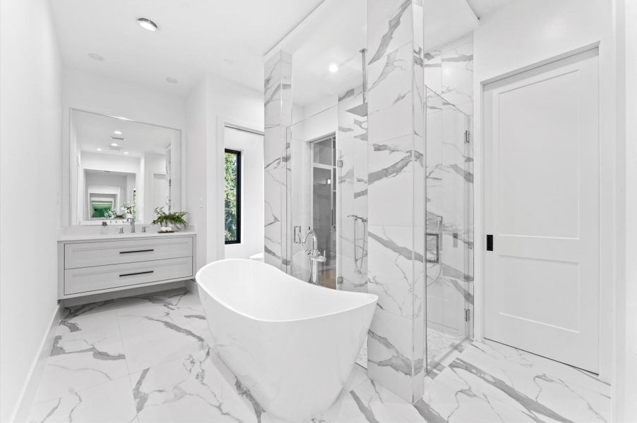 This modern bathroom features a sleek freestanding tub, a spacious walk-in shower with glass doors, and elegant marble-patterned tiles. The room is bright and airy, with a large mirror above the double vanity and a minimalist design.