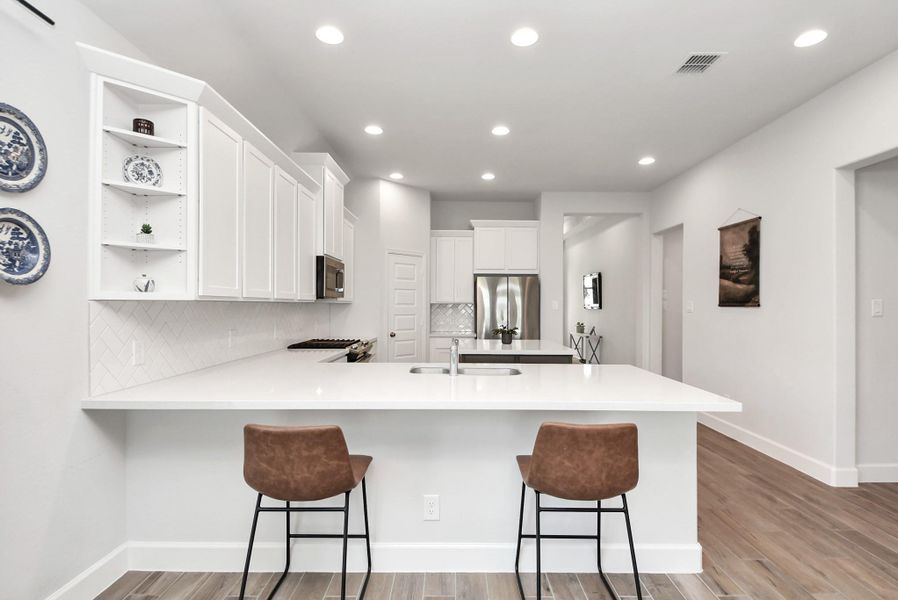 The heart of the home, this modern kitchen showcases sleek countertops, stainless steel appliances, and a central island with seating for two. Recessed lighting and warm wood flooring enhance the inviting ambiance—perfect for cooking, entertaining, or casual gatherings.