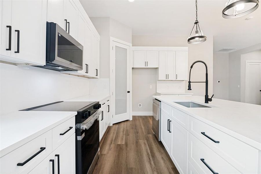 Modern kitchen featuring white cabinetry, quartz countertops, a kitchen island with sink and matte black faucet, stainless steel appliances, and wood-finish flooring