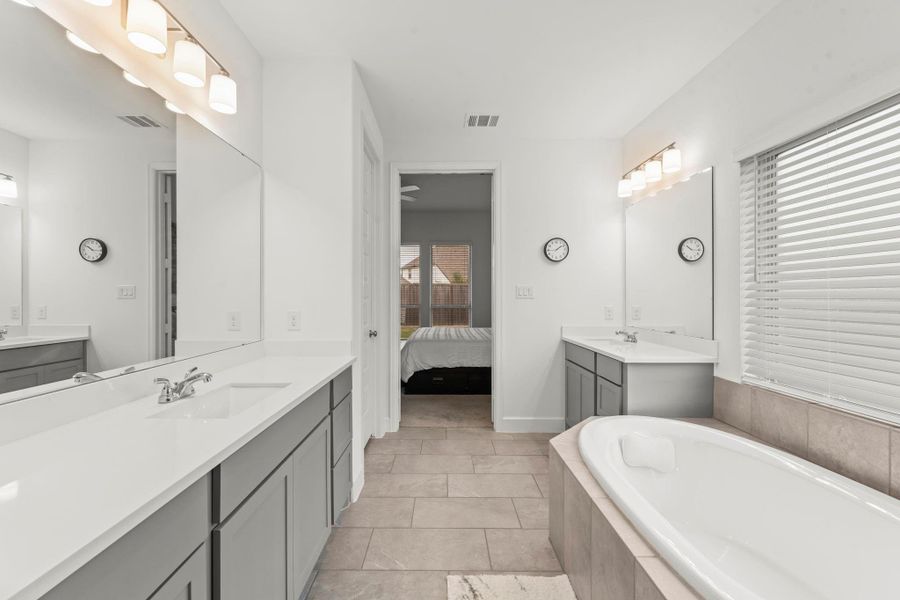 Dual vanities feature rich cabinetry, rectangular undermount sinks, and quartz countertops, thoughtfully placed on separate walls to provide ample space when getting ready. An extended vanity area offers a dedicated space for pampering, while raised-height countertops add everyday comfort. A spacious linen closet and private commode further elevate this well-appointed bath.