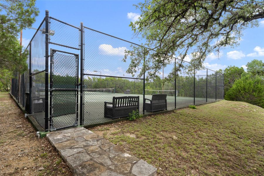A well-maintained tennis court awaits, bordered by secure fencing and a stone pathway. A well-maintained tennis court awaits, bordered by secure fencing and a stone pathway.