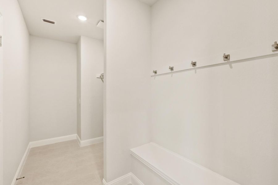 Mudroom with white walls, coat hooks, built-in bench, and carpeted floor leading to a hallway