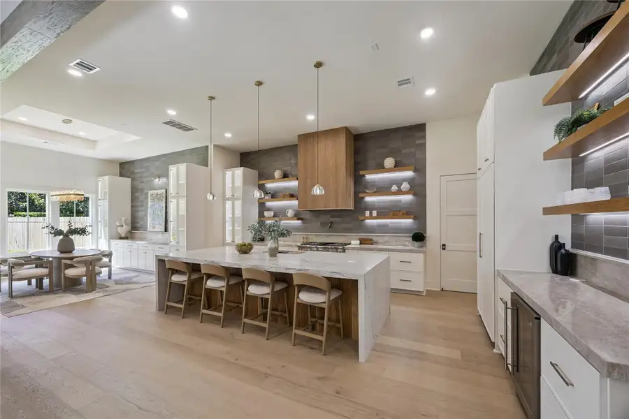 KITCHEN III: A stunning oversized Taj Mahal quartzite island provides abundant seating while designer lighting, illuminated shelving, premium Thermador appliances, and an adjacent dry bar with beverage station elevate this exceptional kitchen.