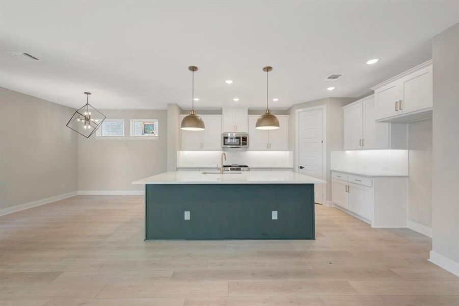 Kitchen with a kitchen island with sink, white cabinetry, light wood finished floors, stainless steel microwave, and a chandelier