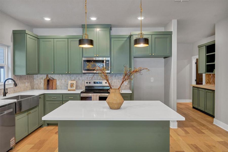 Kitchen featuring green cabinets, backsplash, light stone countertops, appliances with stainless steel finishes, and pendant lighting