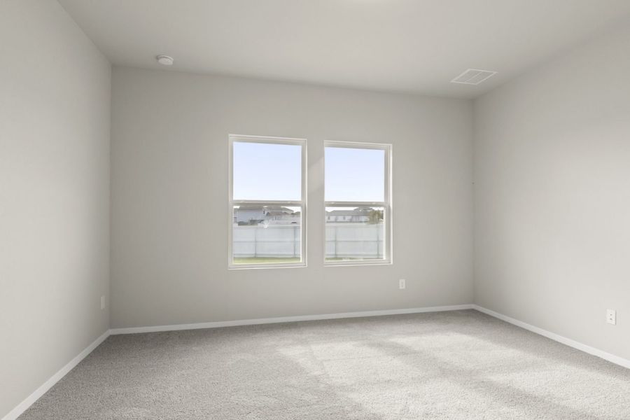 Image of primary bedroom with tan carpeting and light grey walls with two windows