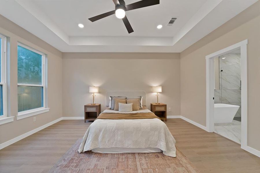 Spacious room featuring wood-finish flooring, a tray ceiling with recessed lighting and a ceiling fan, and dual windows Spacious room featuring wood-finish flooring, a tray ceiling with recessed lighting and a ceiling fan, and dual windows