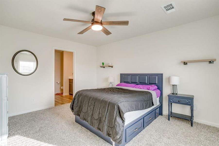 Bedroom featuring ensuite bath, light carpet, and a ceiling fan