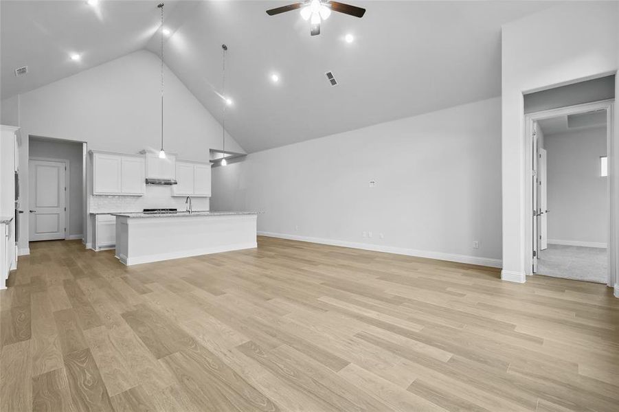 Unfurnished living room featuring ceiling fan, high vaulted ceiling, a sink, light wood-style flooring, and baseboards Unfurnished living room featuring ceiling fan, high vaulted ceiling, a sink, light wood-style flooring, and baseboards