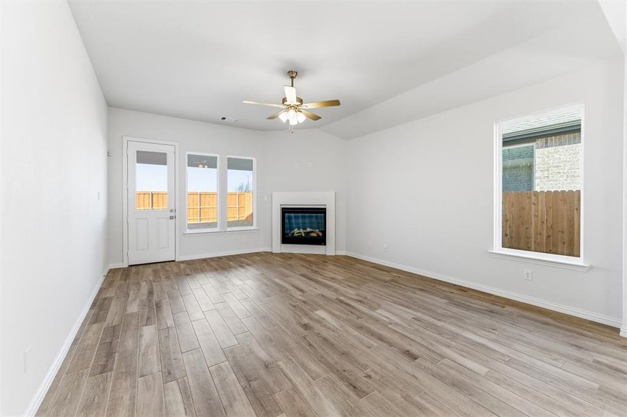 Unfurnished living room with a glass covered fireplace, light wood-style floors, a ceiling fan, and vaulted ceiling