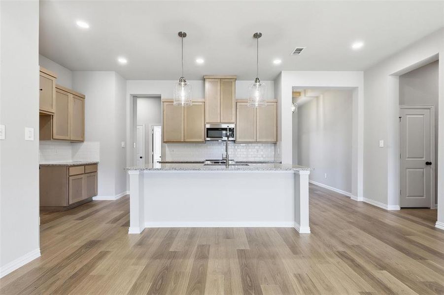Kitchen featuring light brown cabinetry, decorative light fixtures, light stone counters, backsplash, and recessed lighting Kitchen featuring light brown cabinetry, decorative light fixtures, light stone counters, backsplash, and recessed lighting