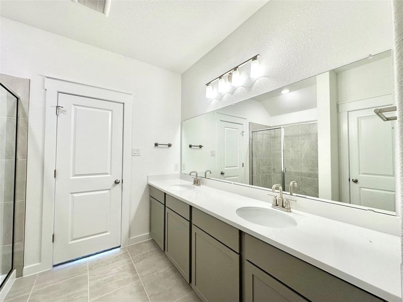 Bathroom featuring double vanity, a stall shower, and light tile patterned floors