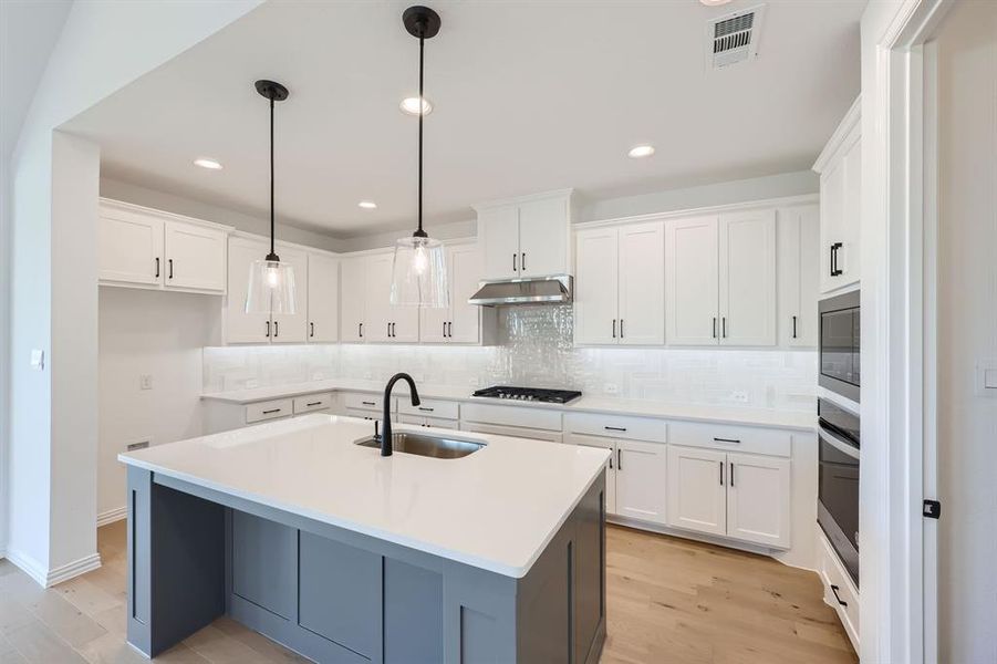 Kitchen featuring decorative backsplash, decorative light fixtures, an island with sink, and white cabinets