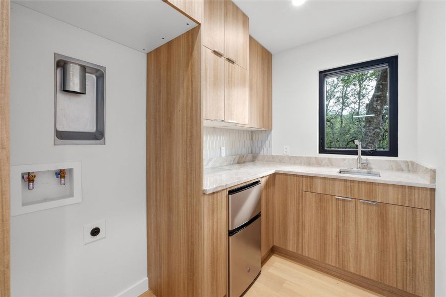 Kitchenette with modern cabinets, a sink, refrigerator, light wood-style flooring, and light stone countersStacked laundry hook-ups