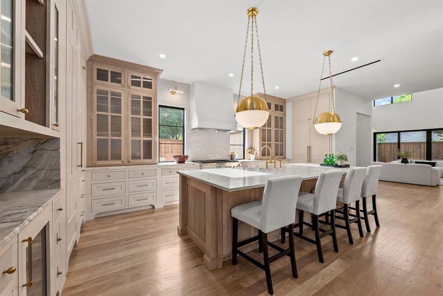 The kitchen features light wood flooring, a central island with white countertops, and seating for four