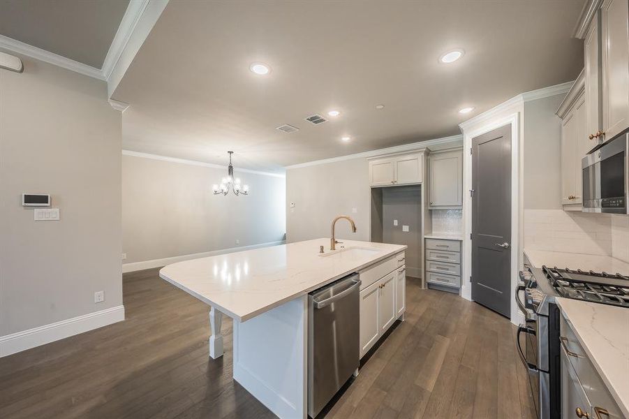 Kitchen featuring a center island with a white countertop and undermount sink, stainless steel dishwasher, gas range, and wood-finish flooring