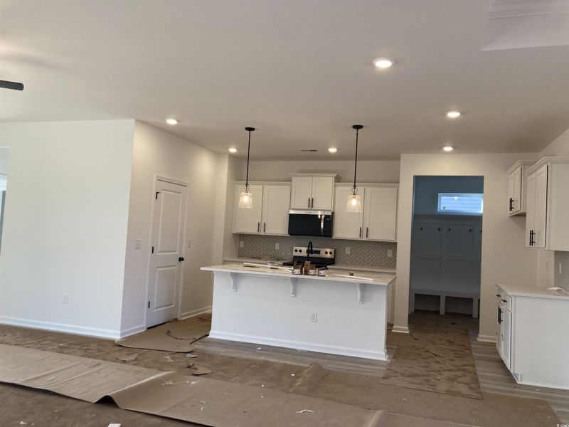 Kitchen featuring a breakfast bar area, tasteful backsplash, hanging light fixtures, white cabinets, and appliances with stainless steel finishes Kitchen featuring a breakfast bar area, tasteful backsplash, hanging light fixtures, white cabinets, and appliances with stainless steel finishes