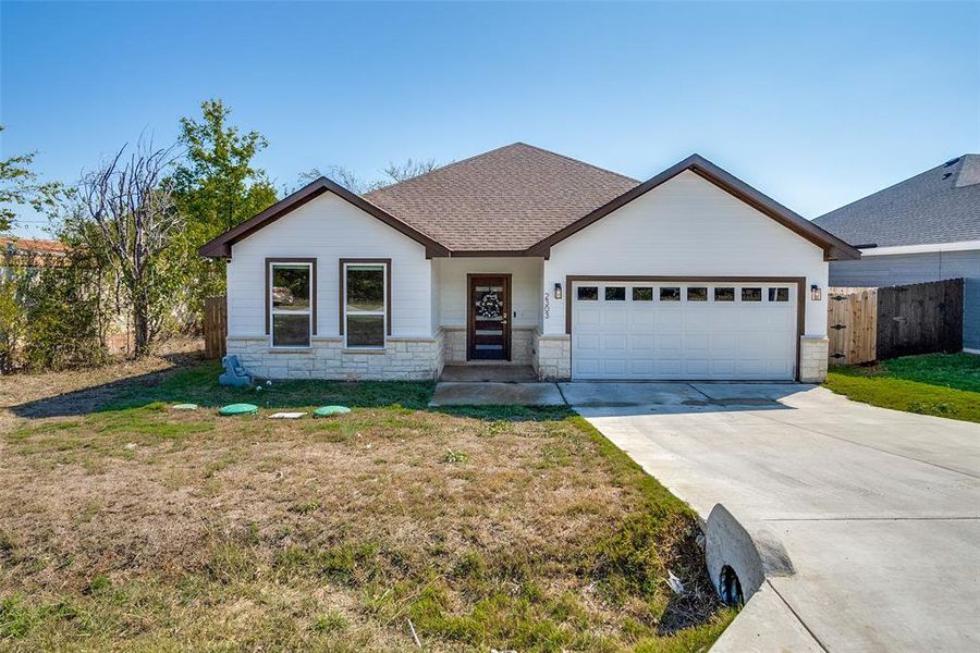 View of front of property featuring stone siding, a shingled roof, concrete driveway, and a garage