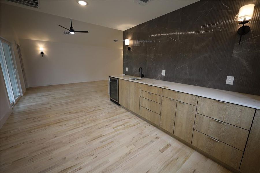 Bar area with modern cabinets, light wood floors, a ceiling fan, beverage cooler, and brown cabinetry