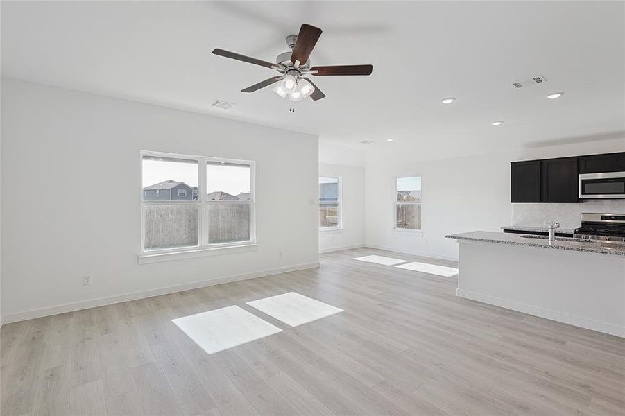 Unfurnished living room with ceiling fan, light wood-type flooring, and sink