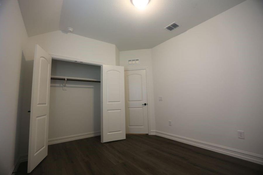 Bedroom featuring wood-finish flooring, white baseboards, a ceiling-mounted light fixture, white walls, and a closet with bifold doors