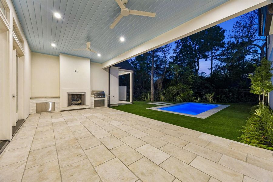 Covered outdoor area with tumbled limestone flooring, gas log fireplace & Blaze outdoor grill. Painted custom ceiling with fans and recessed lighting overlooks the turf & beautiful pool, creating a seamless indoor-outdoor relaxation and/or entertaining space. Go ahead and plan your next Pool Party!