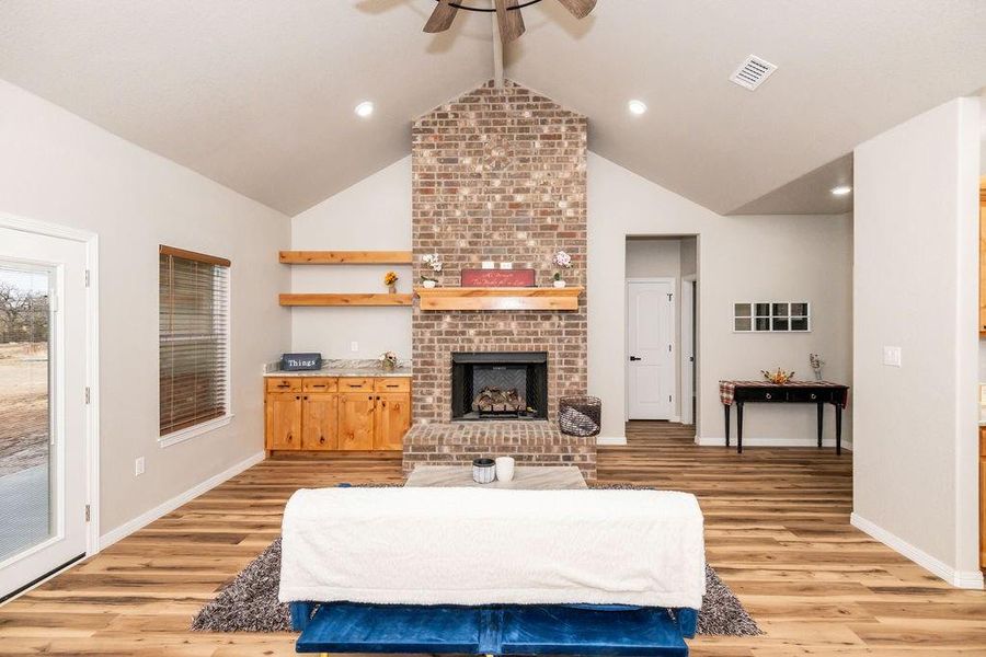 Living room featuring a brick fireplace, vaulted ceiling, light hardwood / wood-style floors, and ceiling fan