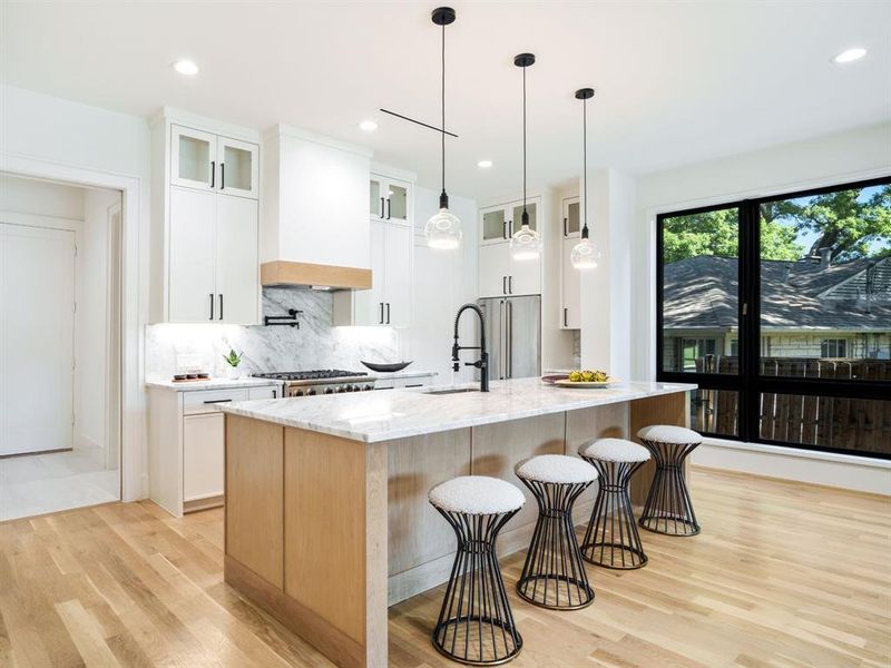 Kitchen featuring glass insert cabinets, decorative light fixtures, light stone countertops, a breakfast bar area, and light wood-style floors