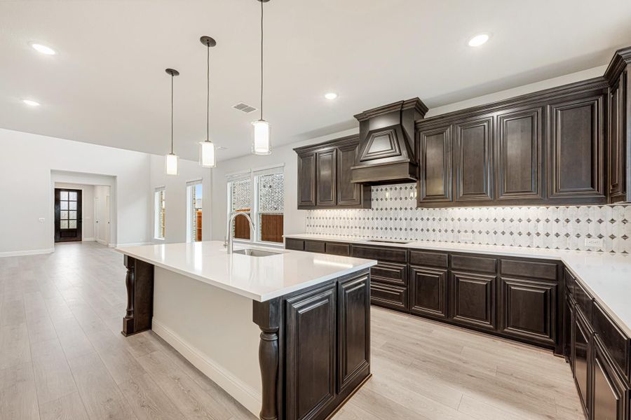Kitchen with dark wood cabinets, large island with white countertops, and patterned tile backsplash