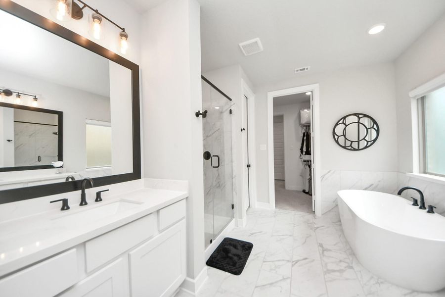 Sleek owner’s bath with black fixtures, large mirror, and closet access.