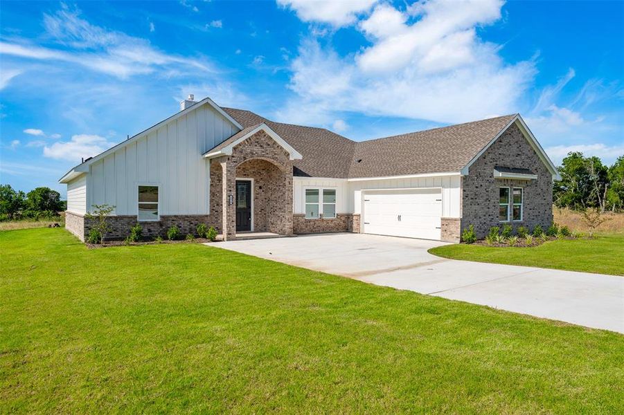 View of front of home featuring board and batten siding, an attached garage, brick siding, driveway, and a front lawn